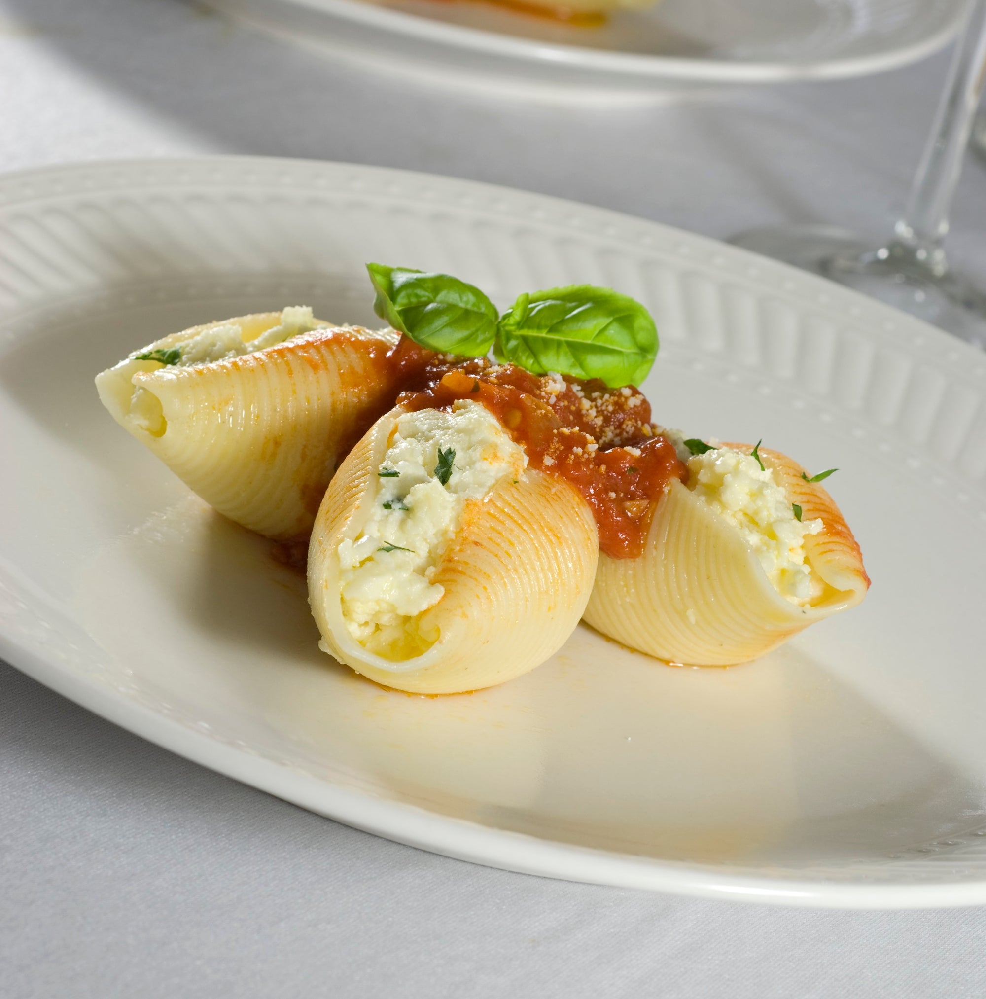 Stuffed pasta shells with a red sauce and basil leaves on a white plate.