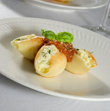 Stuffed pasta shells with a red sauce and basil leaves on a white plate. thumbnail